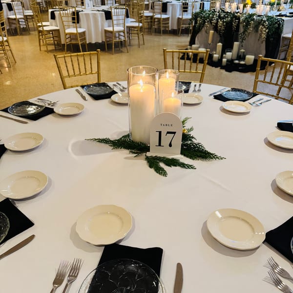 Elegantly set table at Casa D'angelo with white tablecloth, candles, greenery, and gold chairs.
