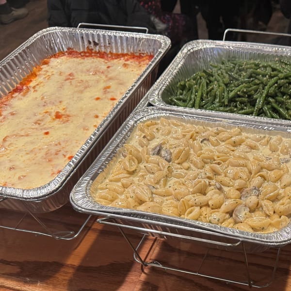 Three catering trays of Italian food: baked ziti, green beans, and pasta shells in cream sauce.