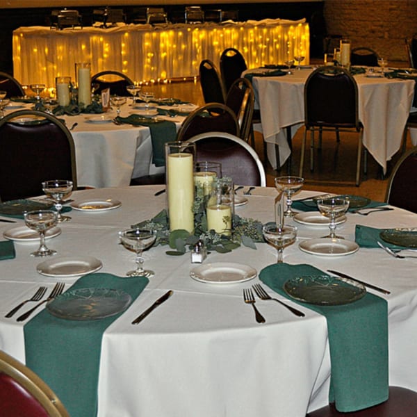 Elegantly set dining tables with white tablecloths, green runners, candles, and sparkling glasses at Casa D'angelo.