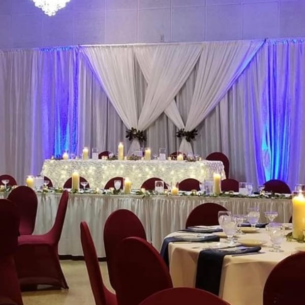 Elegant dining room set for an event with white draped walls, blue uplighting, and candlelit tables.