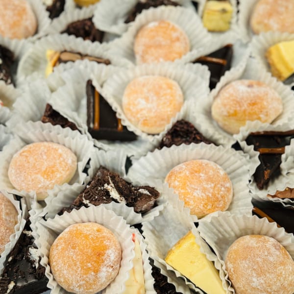Assortment of Italian pastries, including powdered sugar donut holes, chocolate brownies, and cheesecake bites.