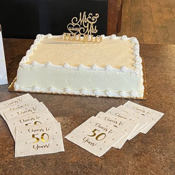 White rectangular anniversary cake with "Mr & Mrs Pellillo" topper and "Cheers to 50 Years!" napkins.