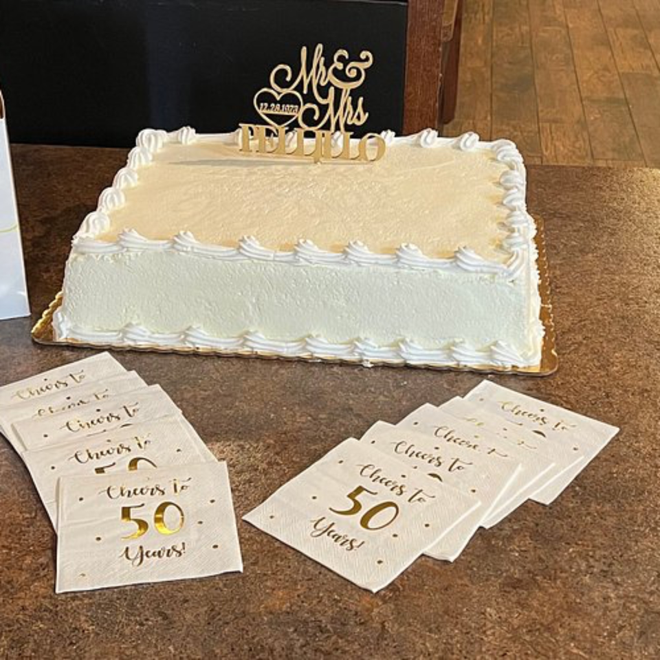 White rectangular anniversary cake with "Mr & Mrs Pellillo" topper and "Cheers to 50 Years!" napkins.