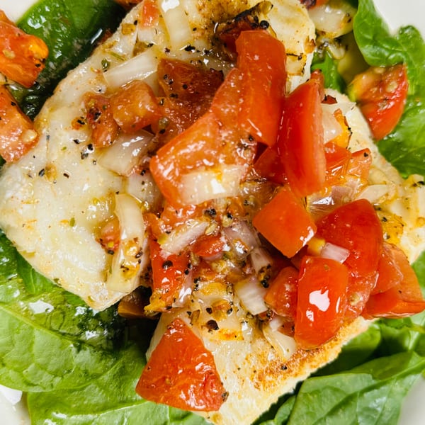 Close-up of grilled fish fillets topped with diced tomatoes and onions, served on a bed of spinach.