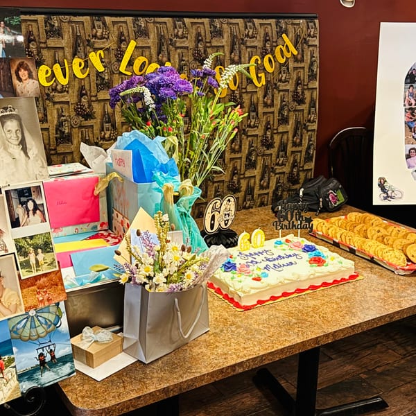A table laden with birthday gifts, flowers, a cake, and cookies, celebrating a 60th birthday.