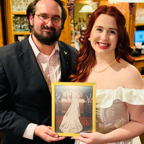 A smiling couple holding a framed photo of a bride in a white wedding dress.