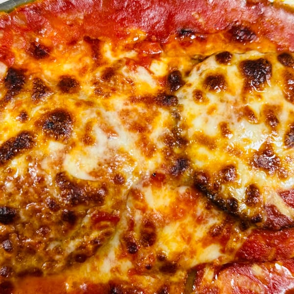 Close-up of a bubbling, cheesy Italian dish with rich red sauce, likely lasagna or baked ziti.