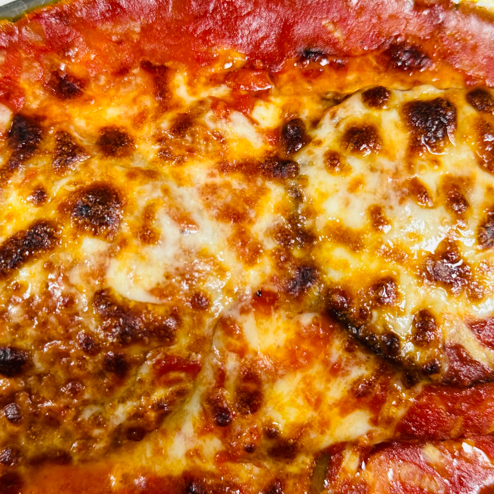 Close-up of a bubbling, cheesy Italian dish with rich red sauce, likely lasagna or baked ziti.