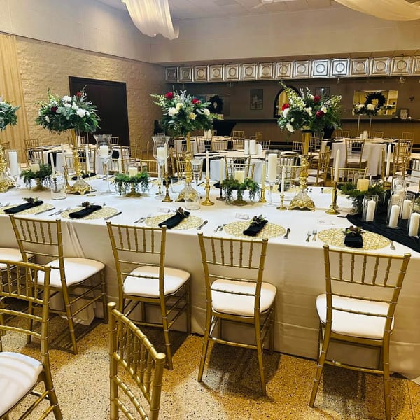 Elegant dining room set for an event with long tables, gold chairs, and floral centerpieces.