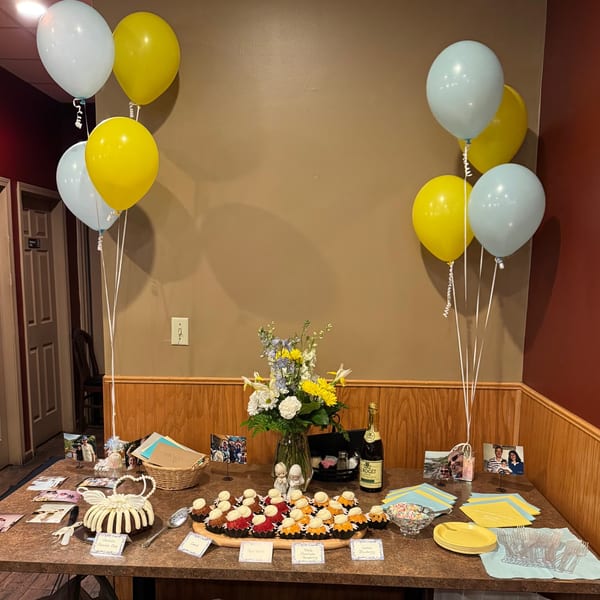 A dessert table with cupcakes, cake, flowers, balloons, and photos for a celebration at Casa D'angelo.