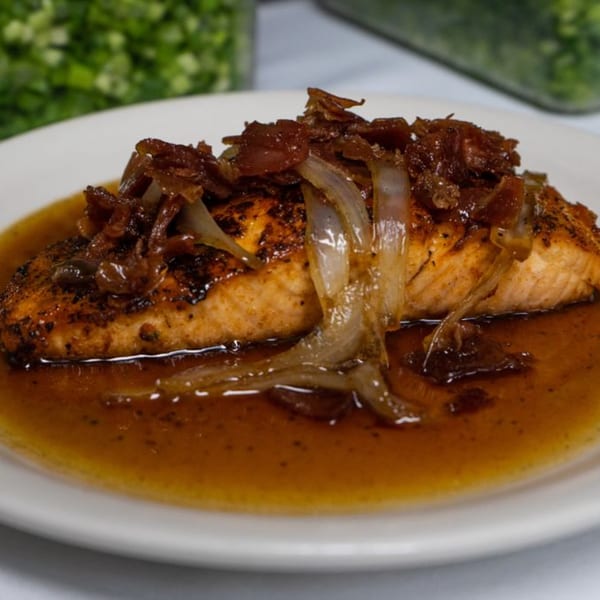 A salmon fillet topped with caramelized onions and a rich brown sauce on a white plate.