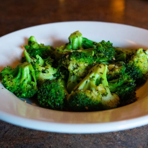 A white plate filled with vibrant green broccoli florets, lightly seasoned with herbs.