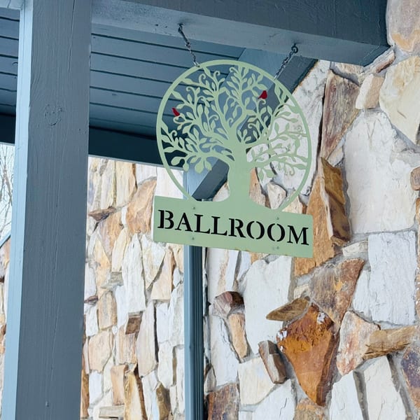 A light green metal sign with a tree design and "BALLROOM" hangs against a stone wall.